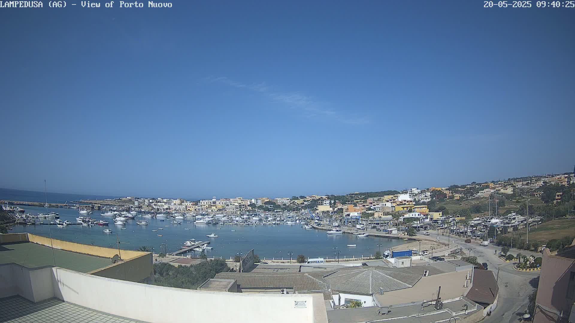 A clear blue sky overlooks a harbor filled with boats, surrounded by a town of low-rise buildings on a sunny day.
