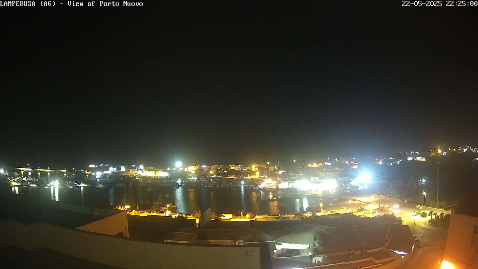 A nighttime view of a harbor filled with boats, surrounded by illuminated buildings under a clear, dark sky.