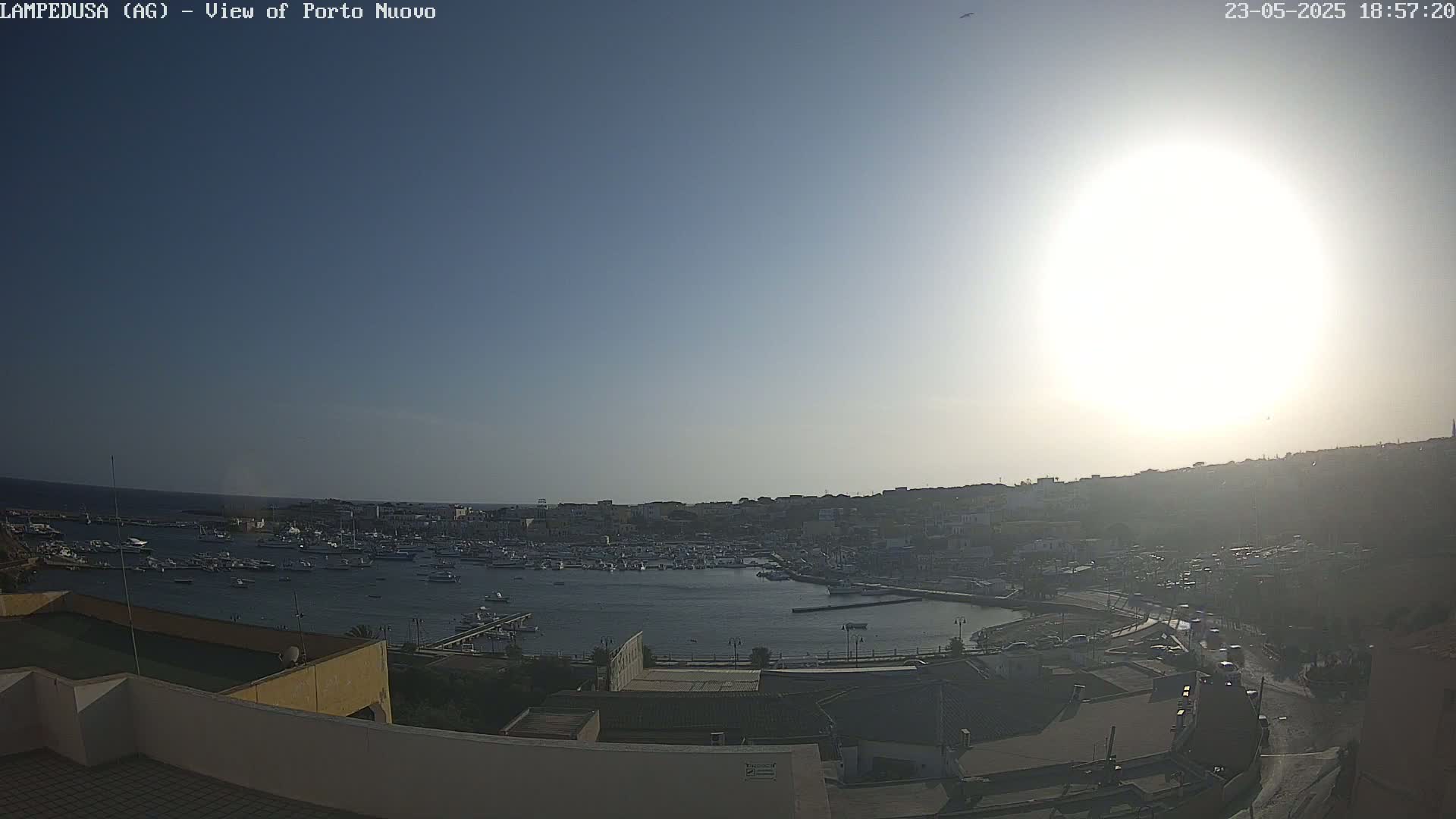 A sunny, bright day overlooks a harbor filled with numerous boats and a town situated on a hillside.