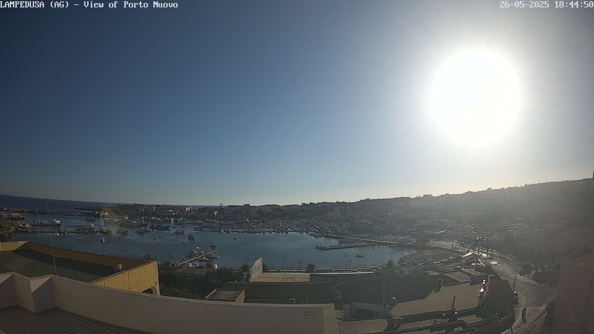 A sunny day overlooks a harbor filled with boats, nestled within a town situated on a hillside.