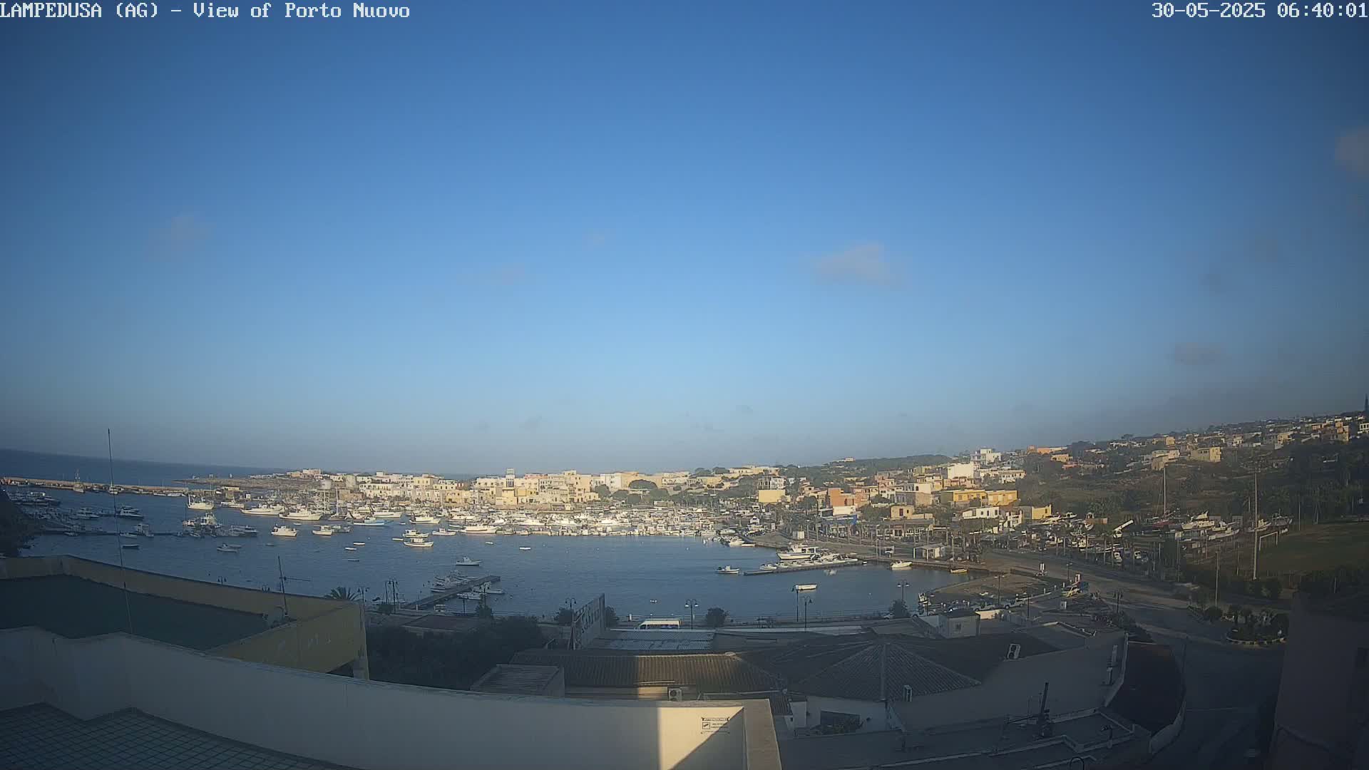 A harbor filled with numerous boats is situated in a town under a clear blue sky.