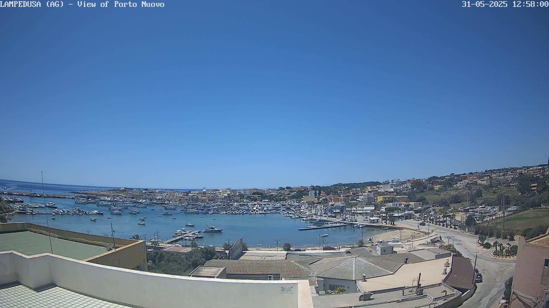 A harbor filled with boats is situated in a town on a sunny day under a clear blue sky.