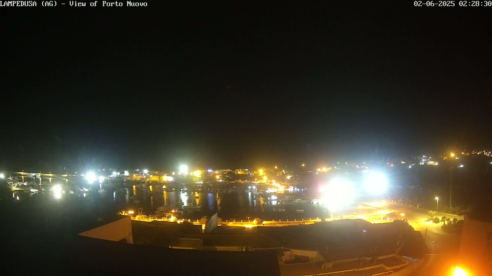 A nighttime, brightly lit harbor scene with many boats and buildings.