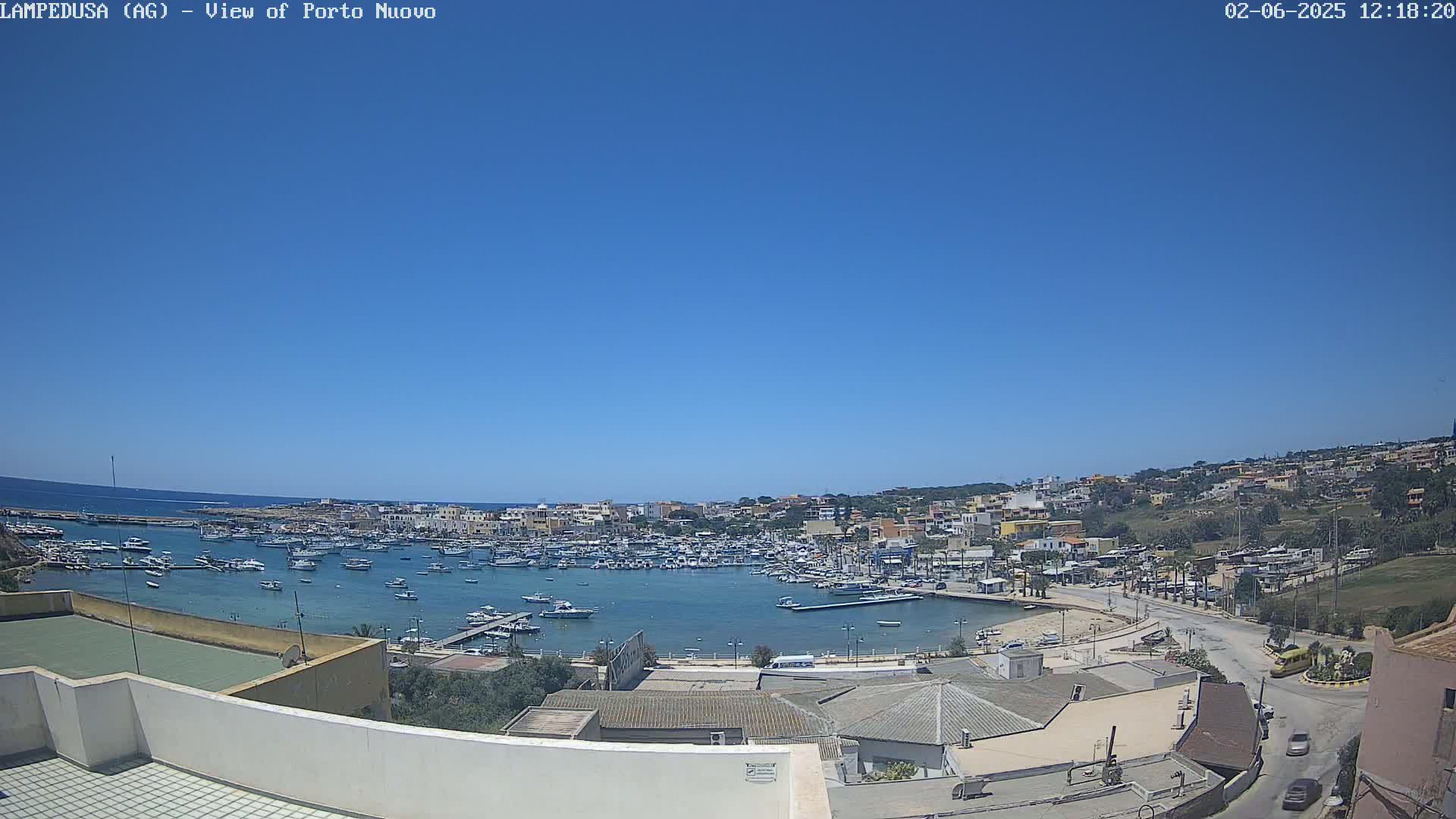 A harbor filled with boats is seen under a clear blue sky, from a high vantage point overlooking a town.