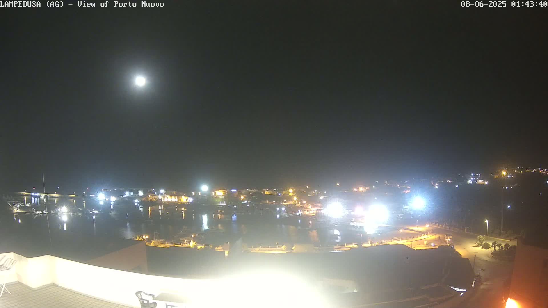 A nighttime view of a harbor town illuminated by lights under a bright moon.