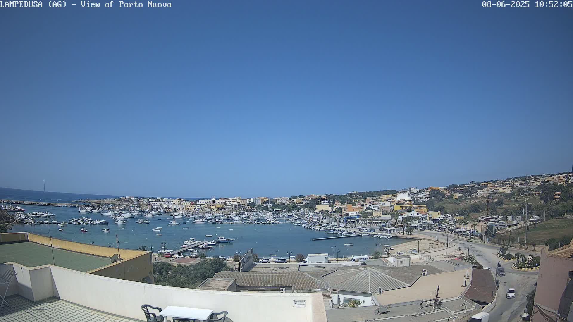 A harbor filled with numerous boats is surrounded by a town of low-rise buildings under a clear blue sky.