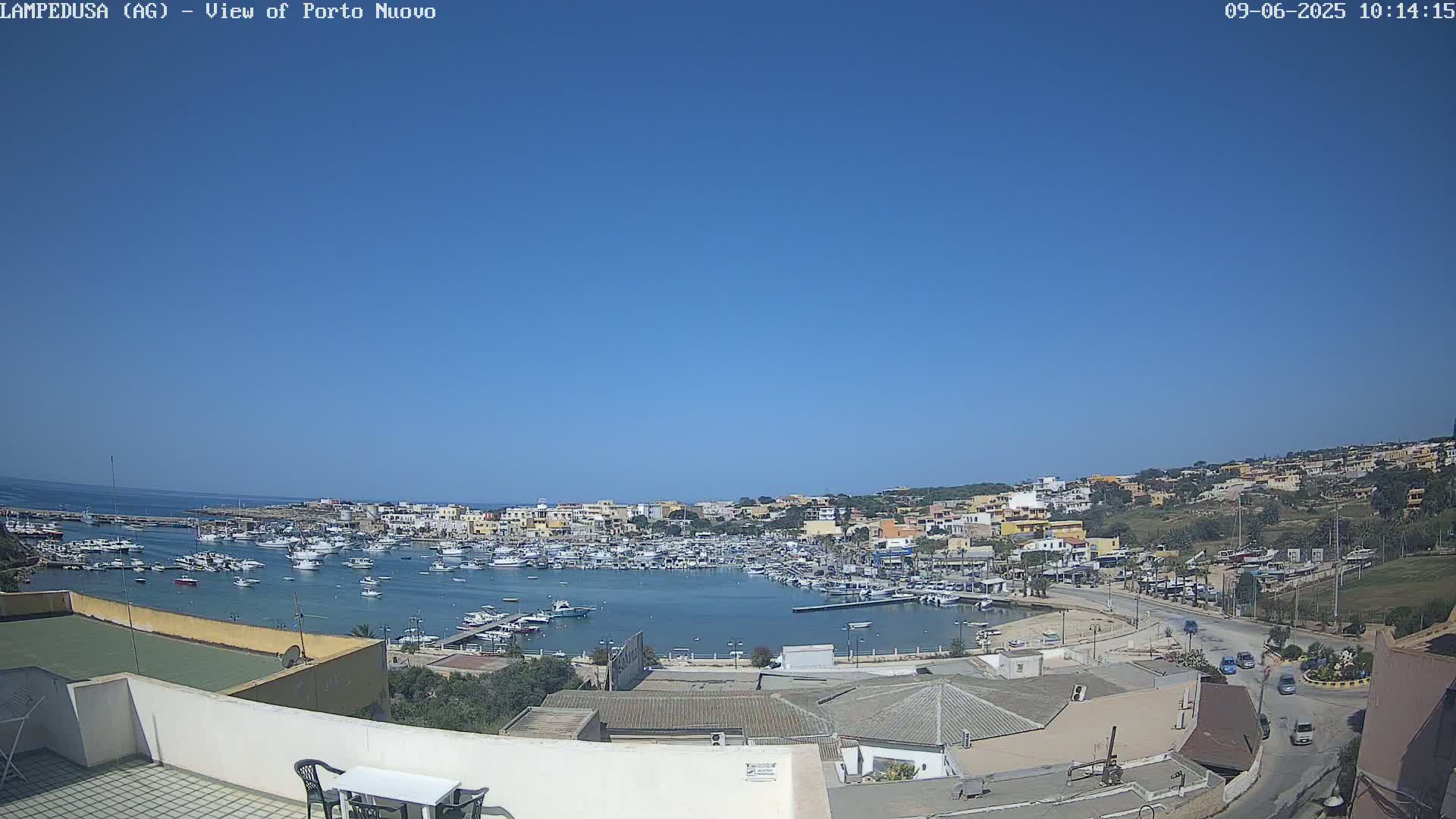 A harbor filled with numerous boats is surrounded by a town of low-rise buildings under a clear blue sky.