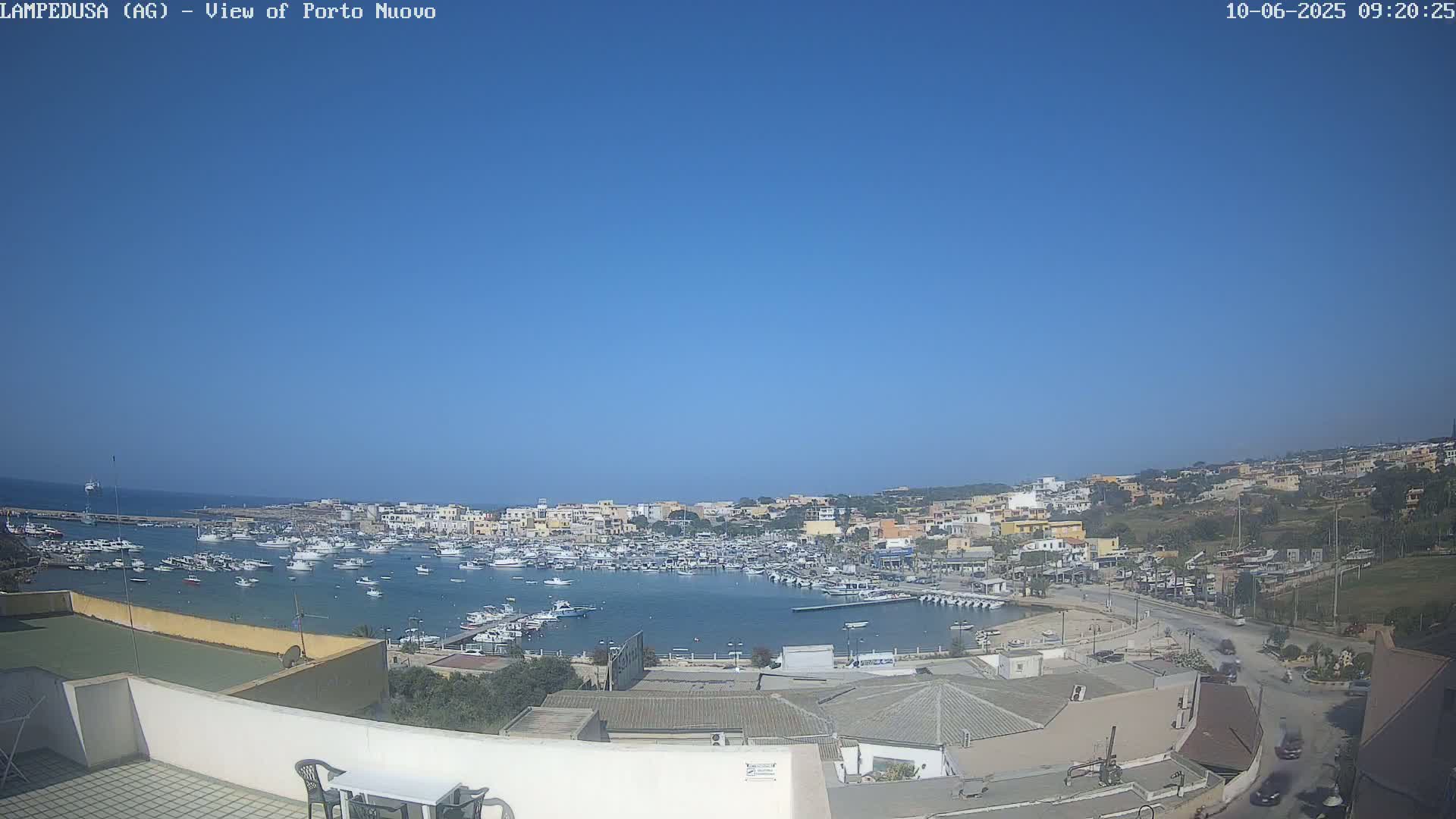 A clear, sunny day overlooks a harbor filled with numerous boats and a town of low-rise buildings that extend uphill.