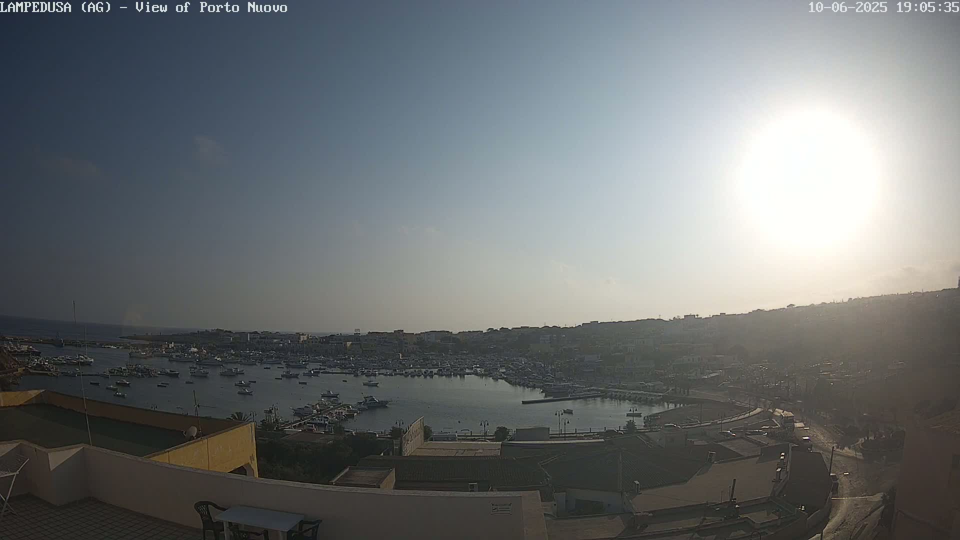 A harbor filled with numerous boats is seen from an elevated viewpoint on a sunny day.