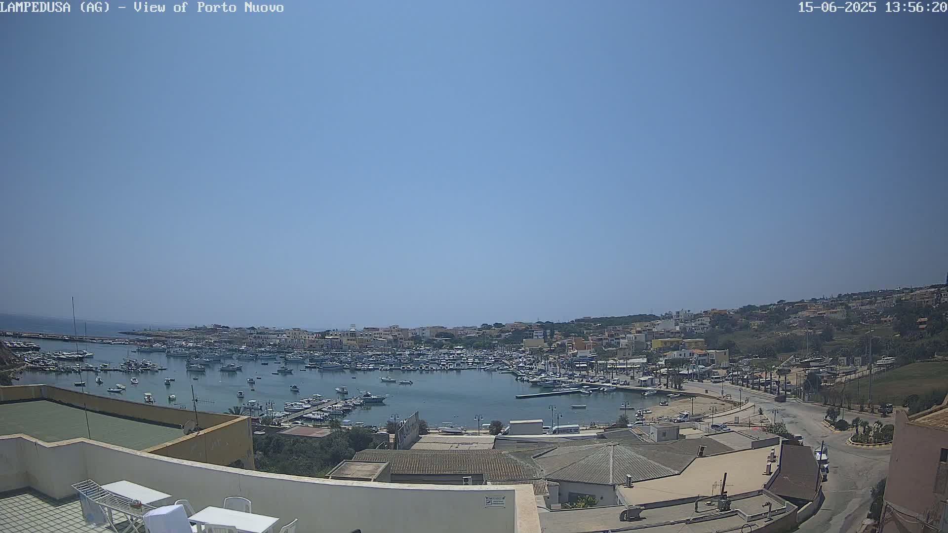 A sunny, clear day overlooks a harbor filled with many boats, adjacent to a town built on a hillside.
