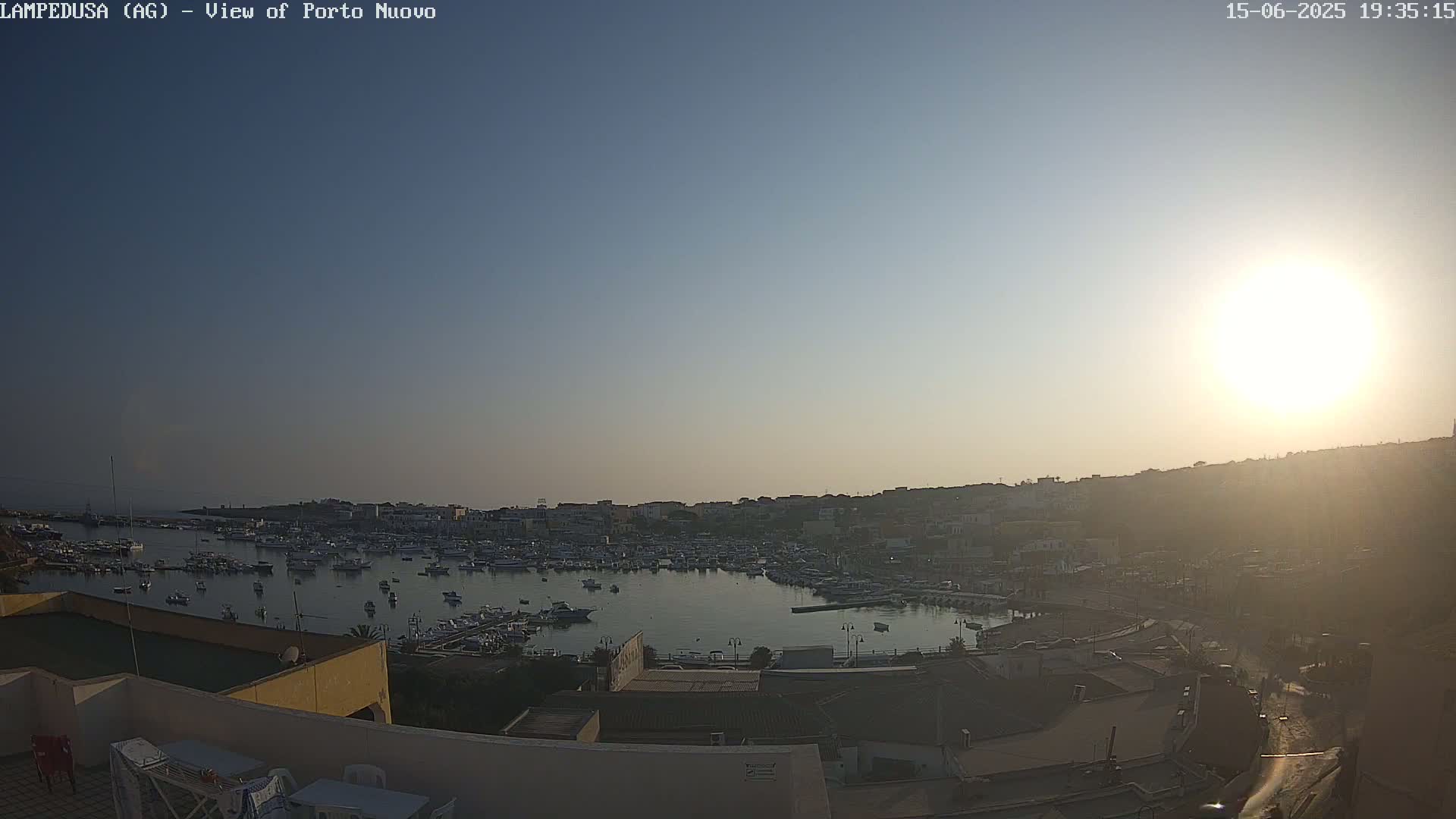 A harbor filled with numerous boats is seen at sunset under a clear sky.