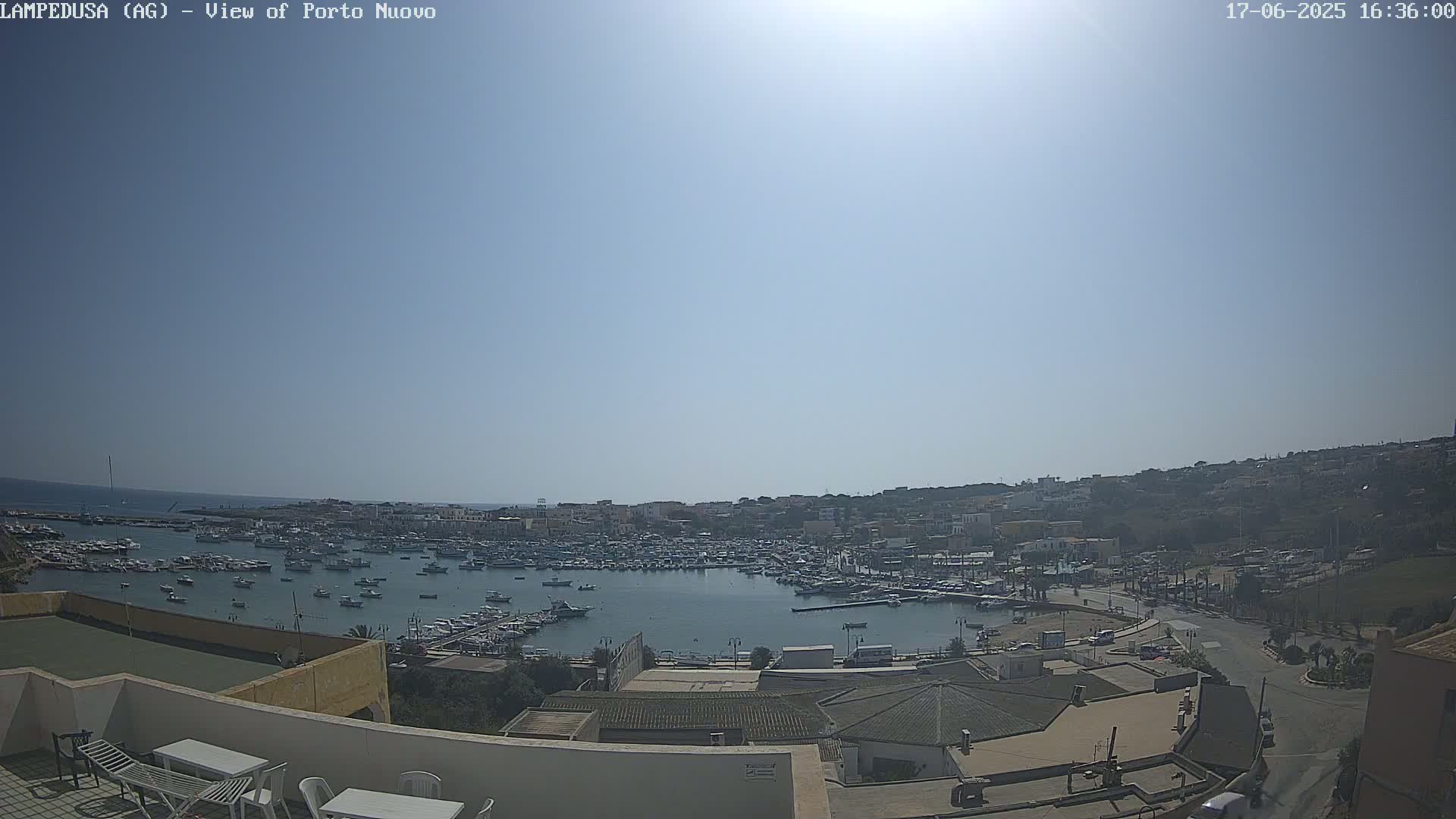 A sunny day overlooking a harbor filled with numerous boats, adjacent to a town built on a hillside.