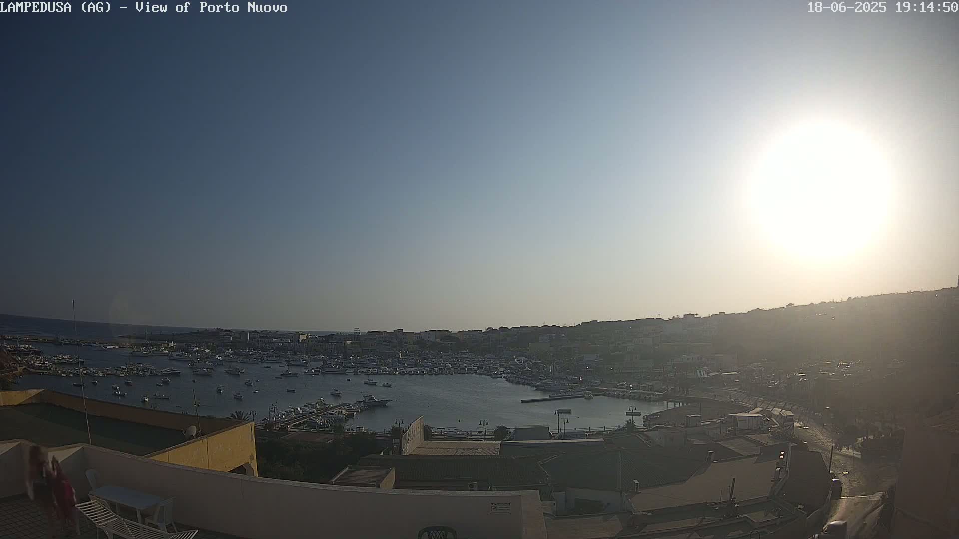 A harbor filled with numerous boats is visible under a bright, sunny sky.