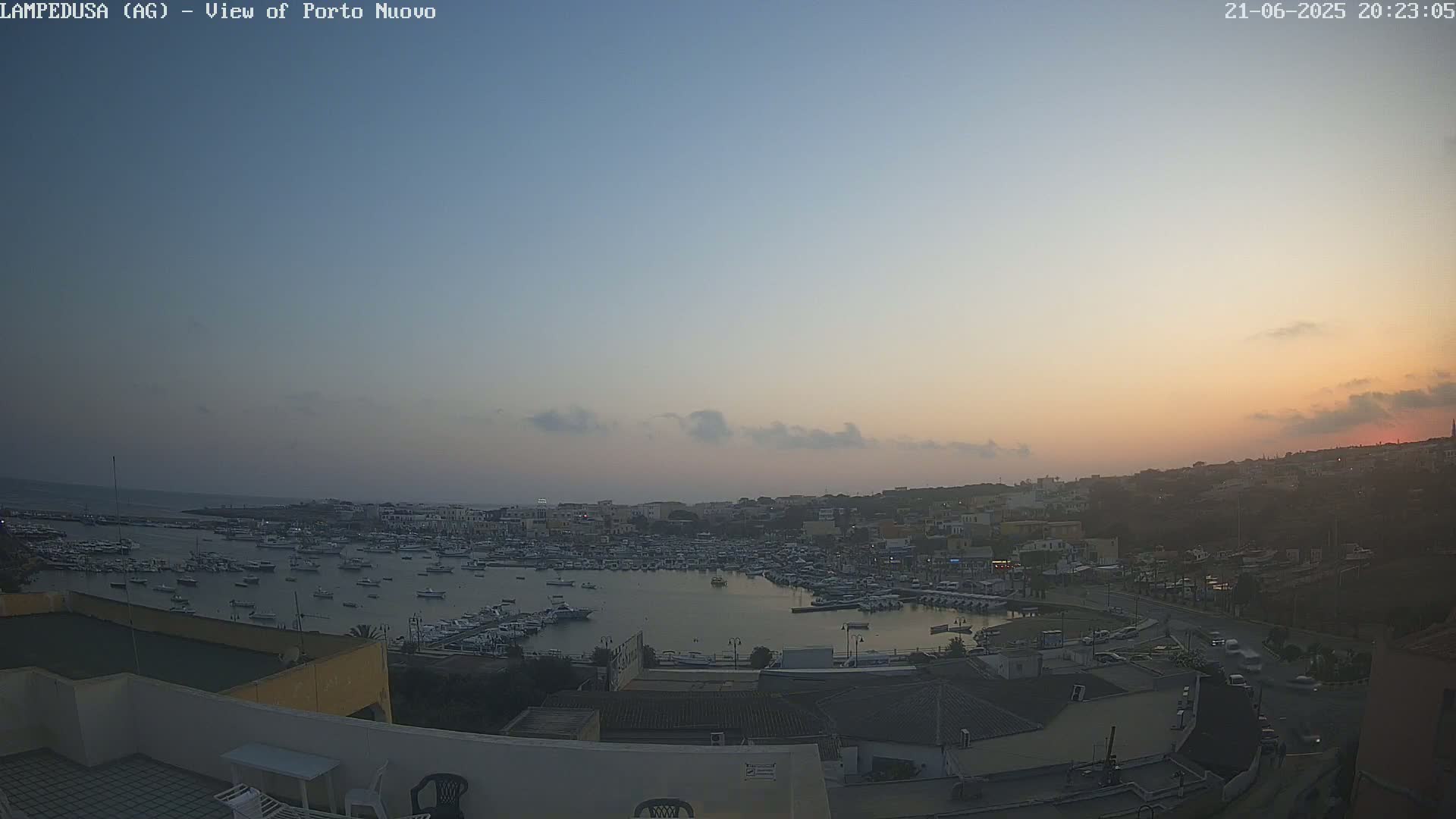 A harbor filled with numerous boats is visible at sunset under a mostly clear sky.