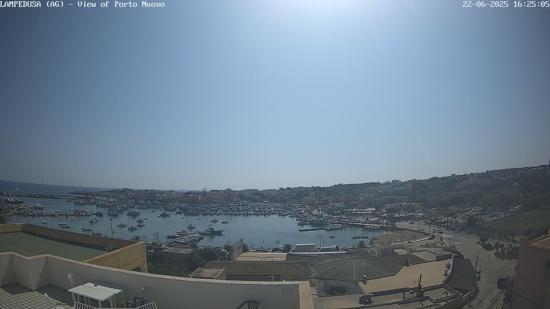 A sunny, clear day overlooks a harbor filled with numerous boats and a town nestled on a hillside.