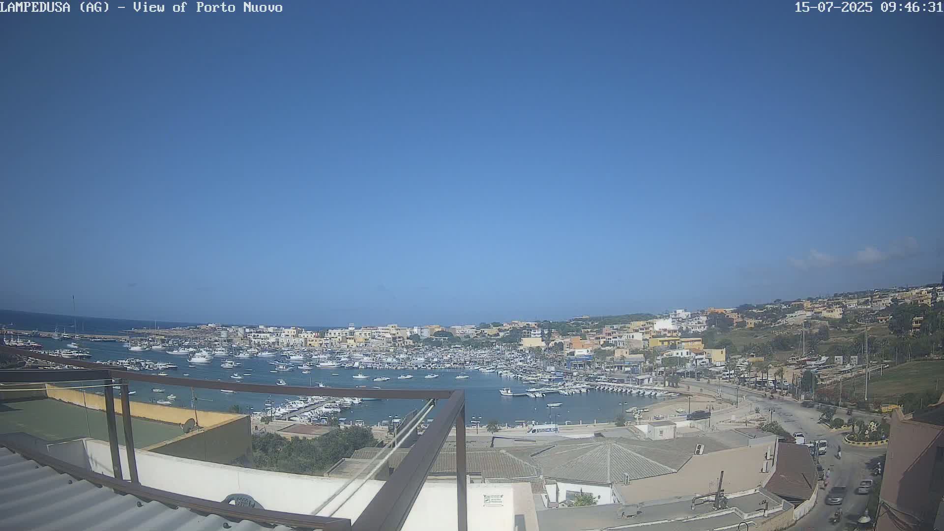 A harbor filled with numerous boats is situated beneath a clear blue sky, overlooking a town built on a hillside.