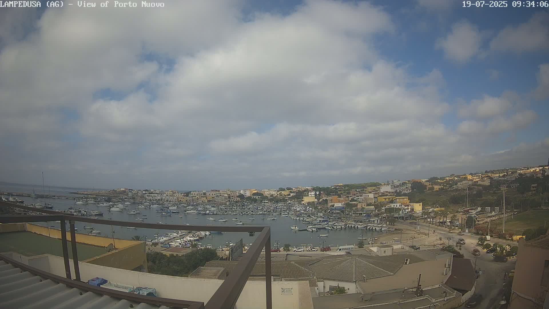 A partly cloudy sky overlooks a harbor filled with many boats and a town built on a hillside.