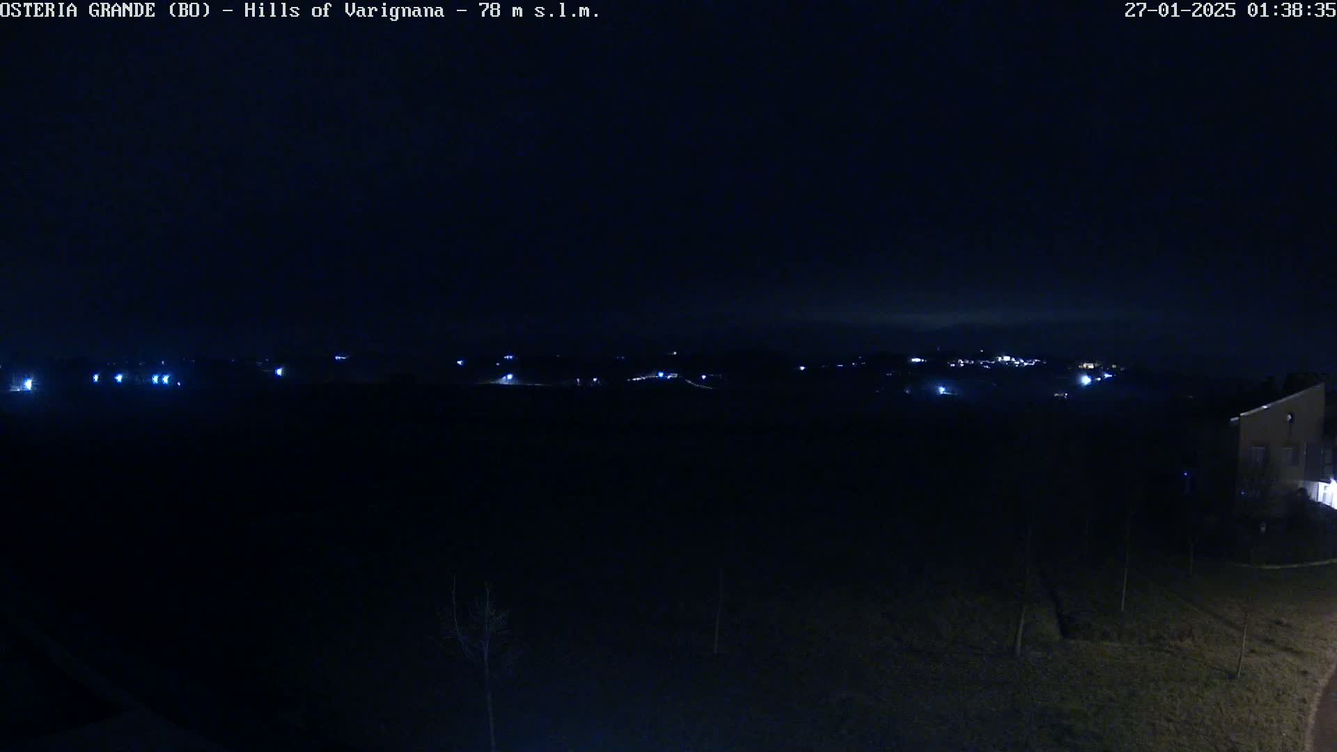 A nighttime long shot shows a dark landscape with a few distant lights in the hills under a clear, dark sky.