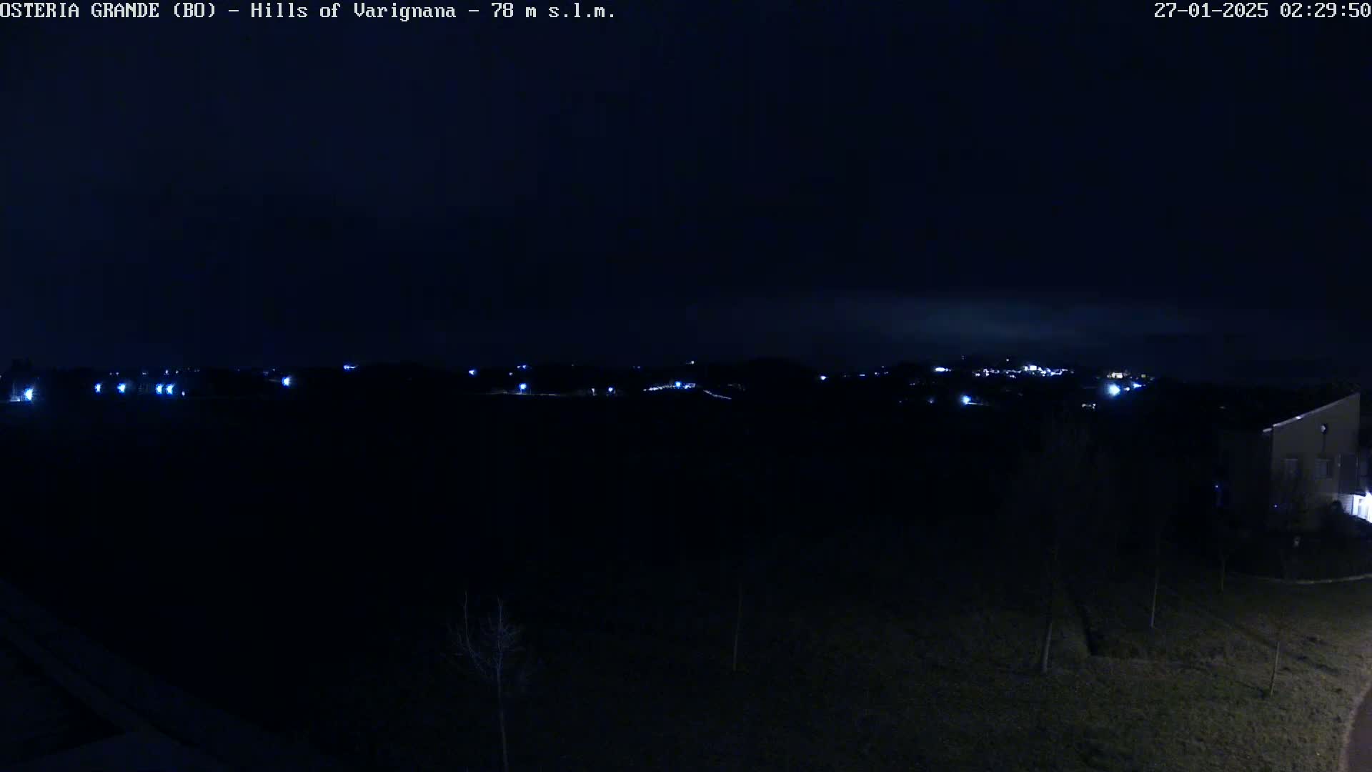 A nighttime, long shot shows faintly lit hills in the distance under a dark sky.