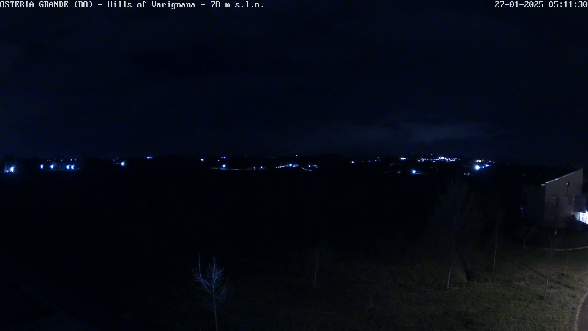 A nighttime view of dimly lit hills and a few buildings under a dark sky.