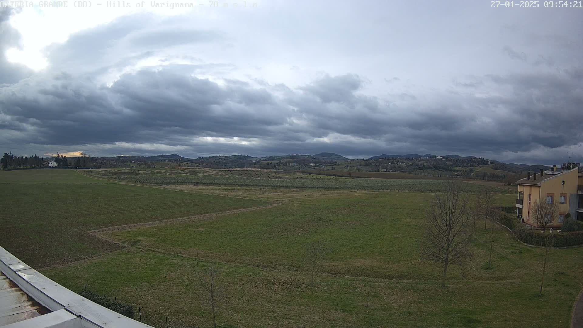 A wide, flat expanse of green fields stretches towards rolling hills under a cloudy sky.