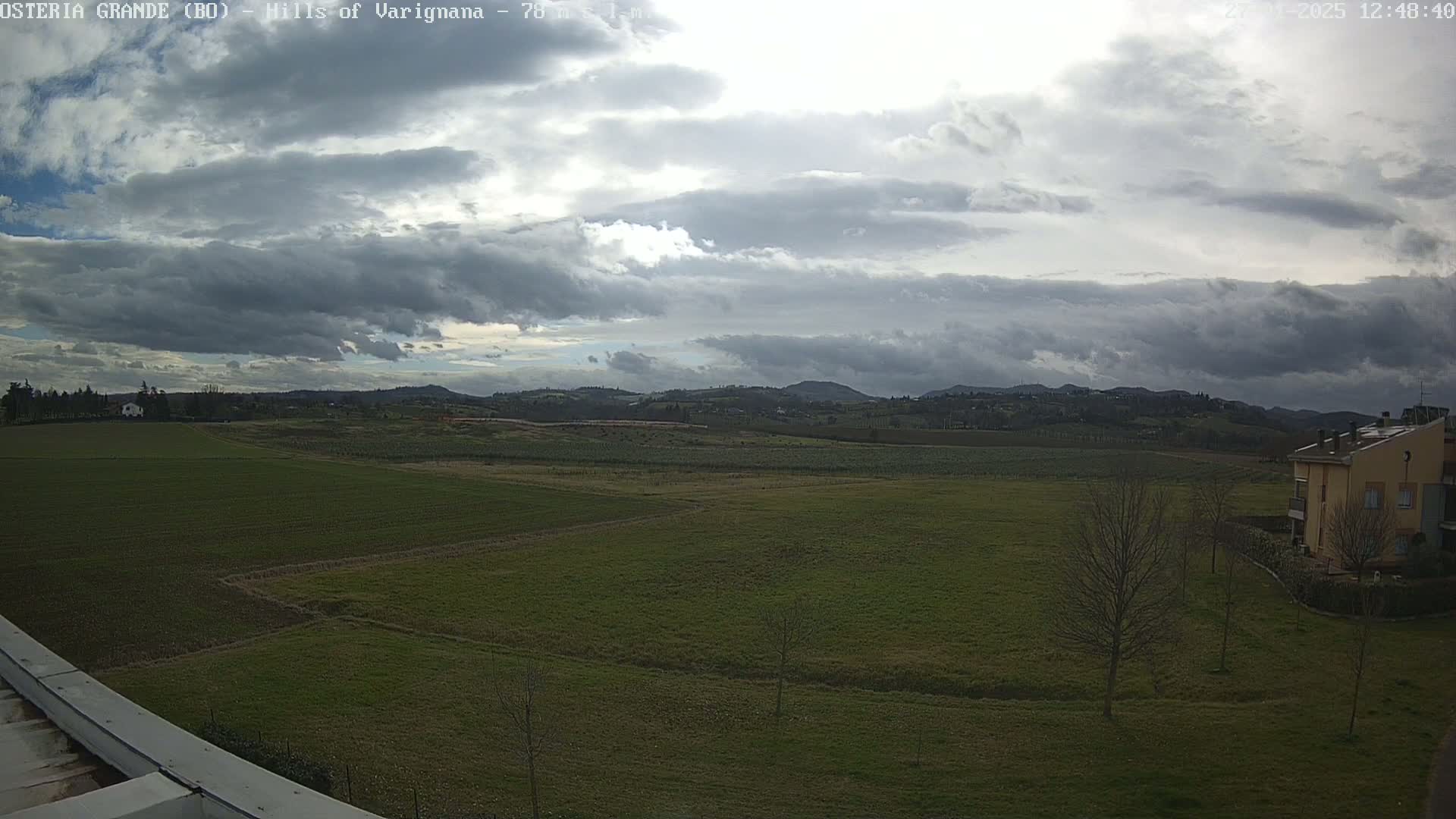 A wide, flat expanse of green fields stretches towards a line of rolling hills under a mostly cloudy sky.