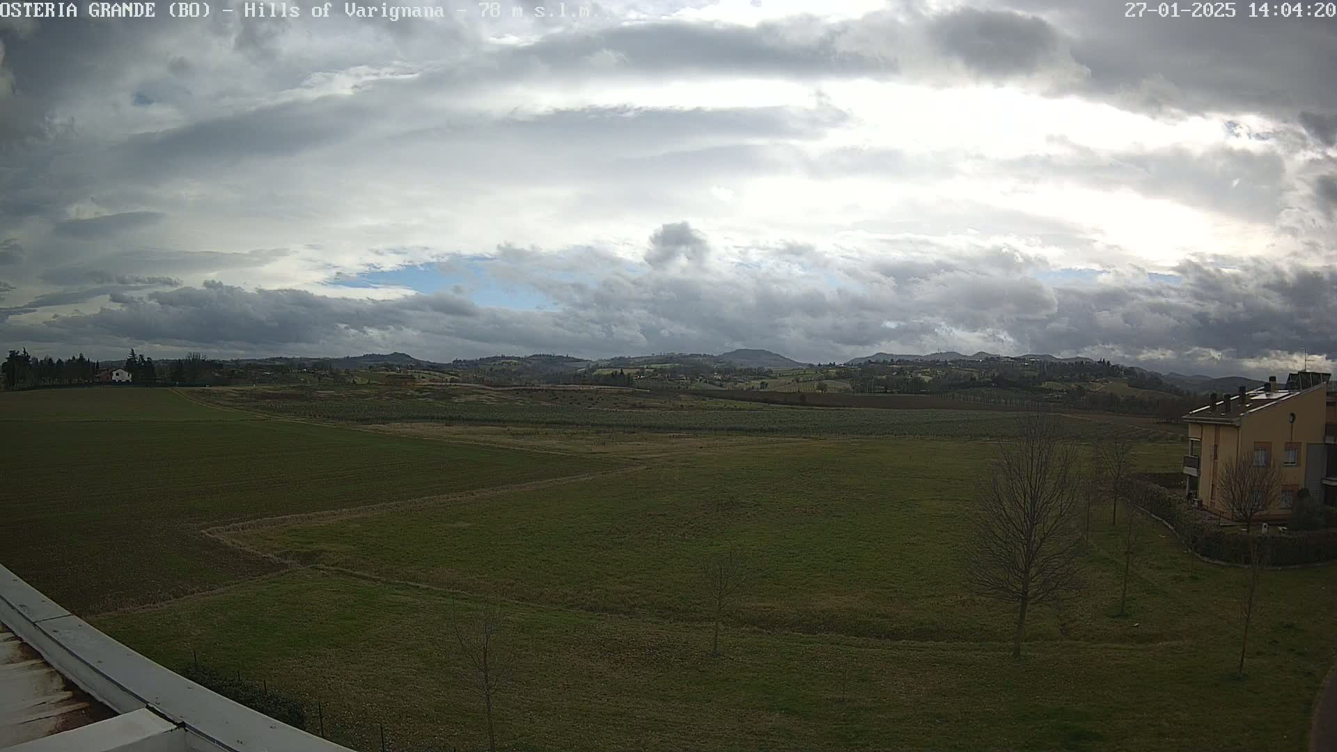 A wide, flat expanse of green farmland stretches to rolling hills under a partly cloudy sky.