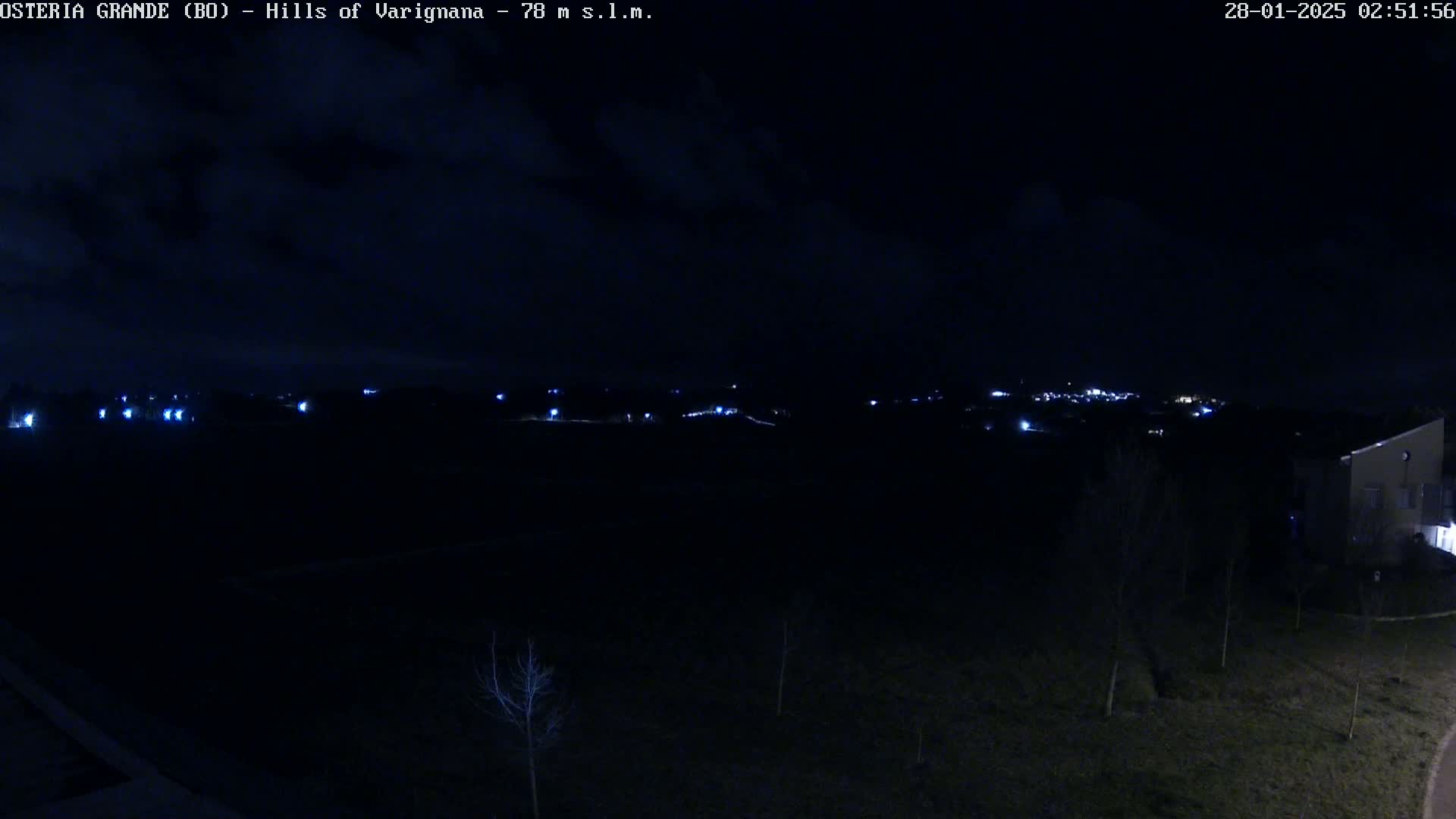 A nighttime view of sparsely lit hills and a small town in the distance under a partly cloudy sky.