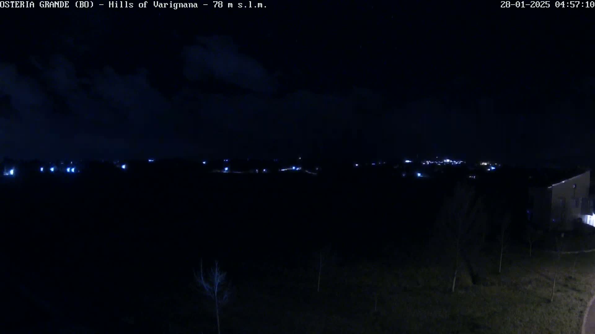 A nighttime, dark view shows a distant line of faint lights across a dark landscape under a mostly clear, dark sky.