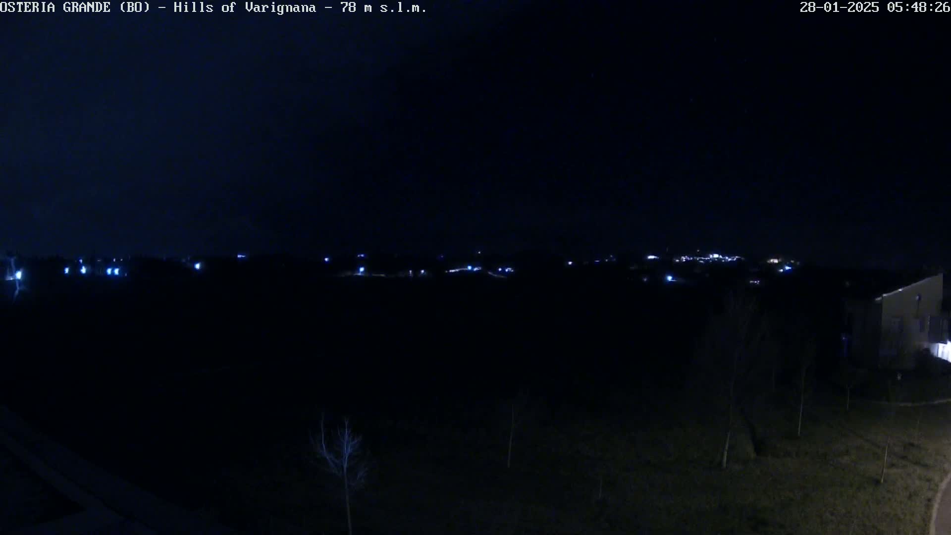 A nighttime, dark view of a sparsely lit landscape with a distant town visible on the horizon.