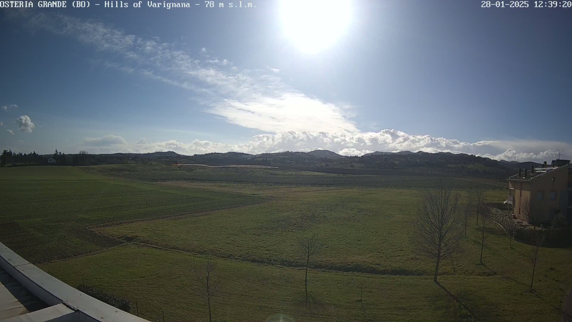 A sunny day with partly cloudy skies over a vast expanse of green fields and rolling hills, in the distance a few buildings are visible.