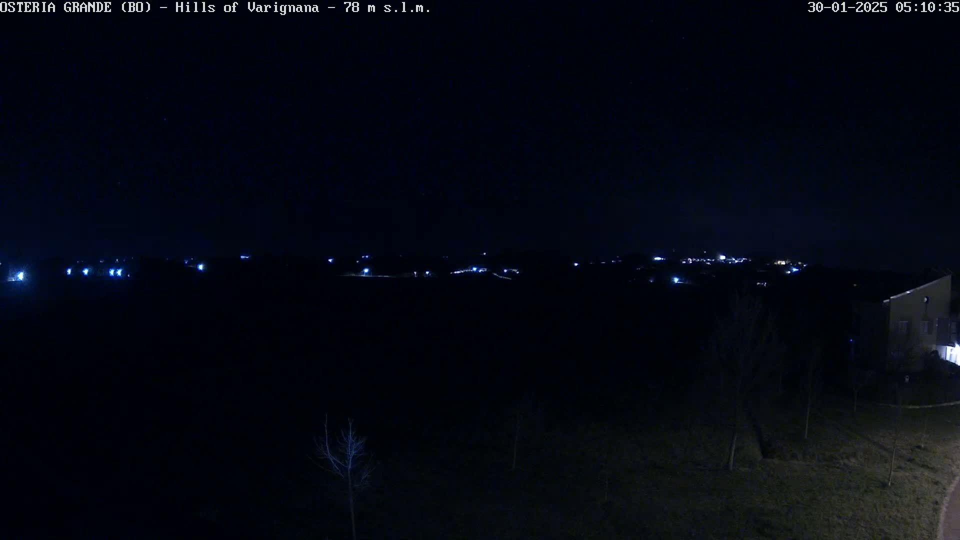 A dark, nighttime view of a sparsely lit landscape with a distant town visible on the horizon, under a clear, starlit sky.