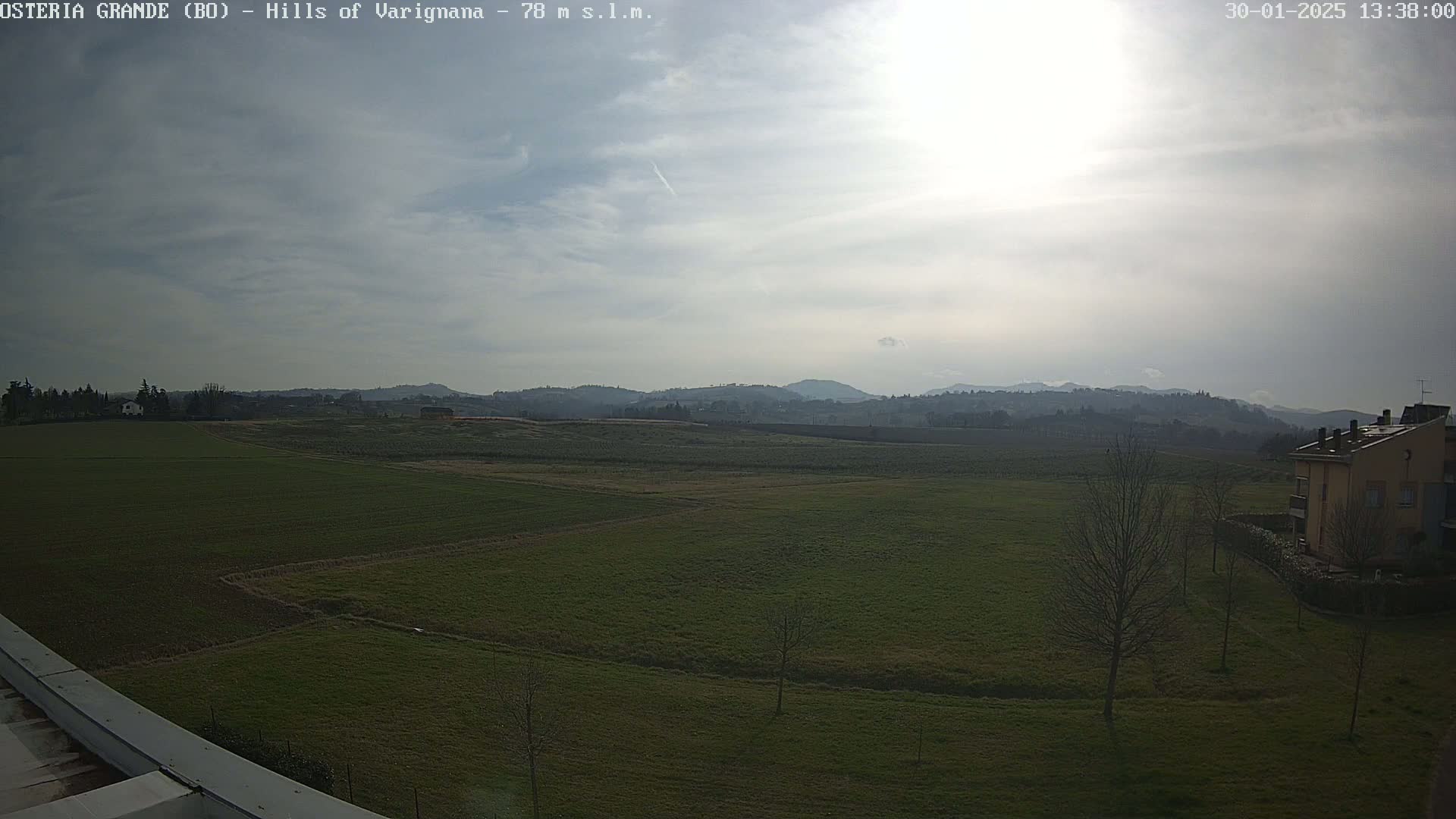 A partly cloudy day reveals a wide expanse of flat, green farmland stretching towards distant, hazy hills.