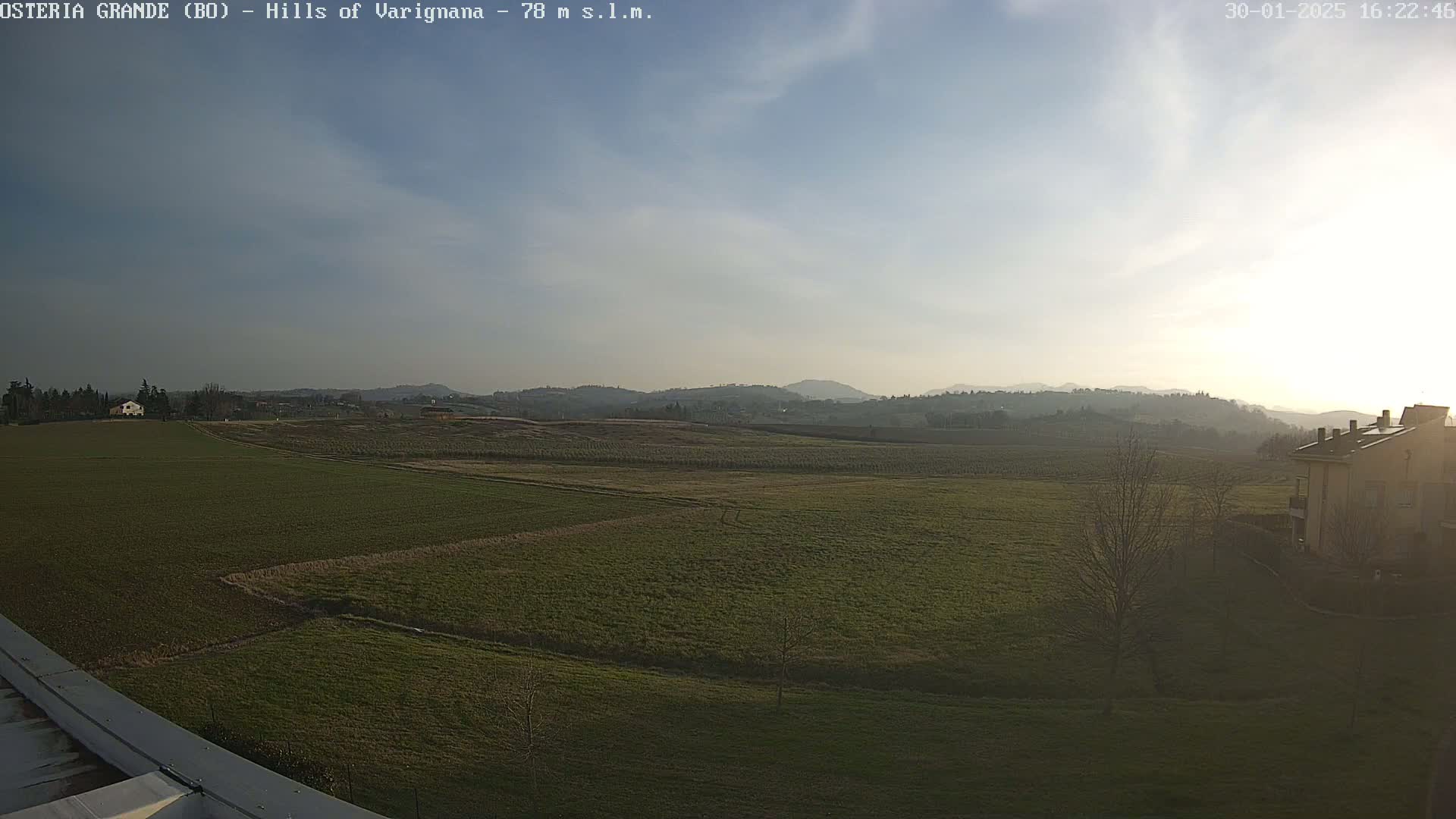 A partly sunny day reveals a sprawling landscape of green fields and distant hills, with a few buildings visible in the foreground and background.