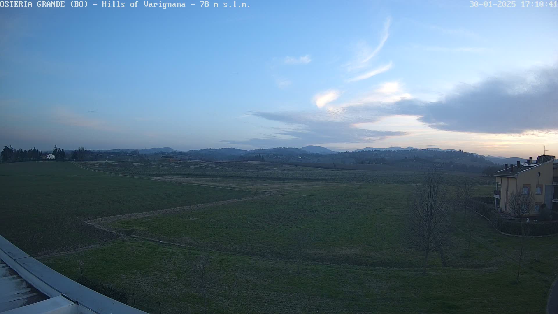 A wide, flat expanse of green fields stretches to distant, rolling hills under a mostly clear, twilight sky.