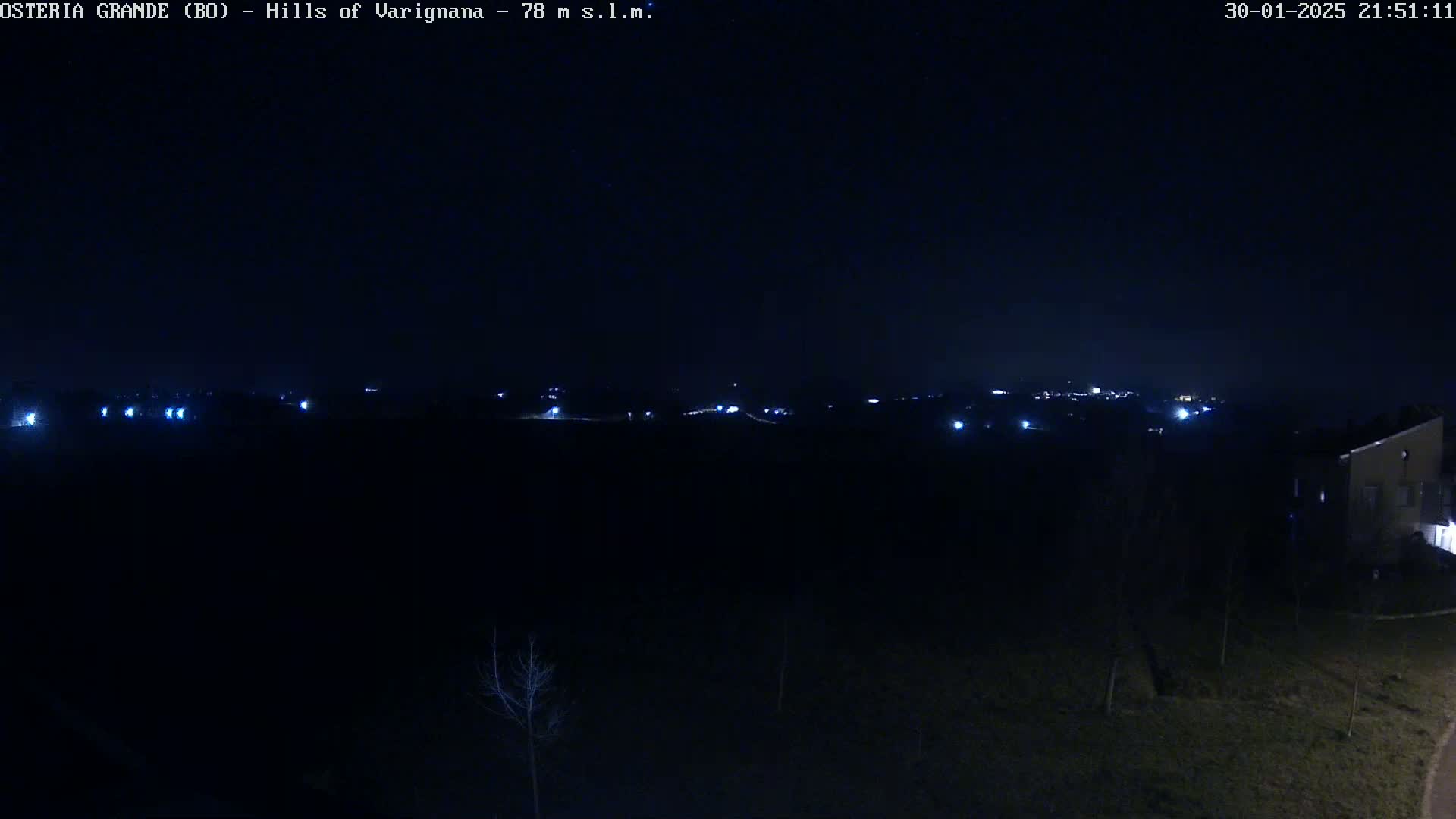A dark, nighttime landscape shows a distant line of faint lights from a town or village, under a clear, dark sky.