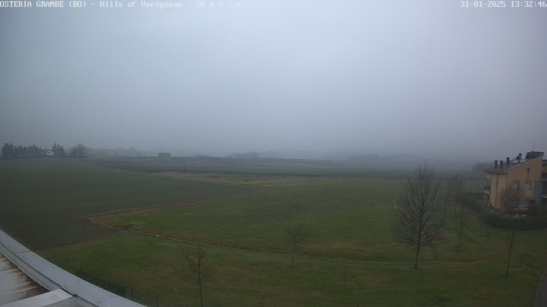 A foggy, flat landscape of green fields, a few sparse trees, and a building in the distance is visible from an elevated vantage point.