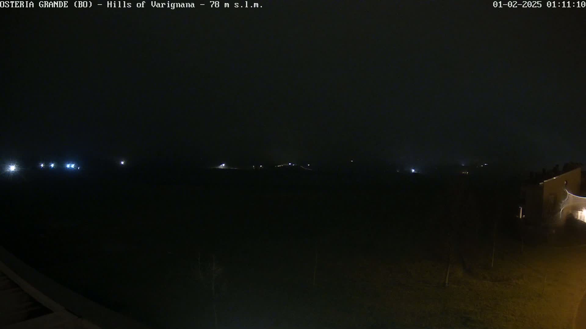 A dark, nighttime landscape is visible, with a few faint lights in the distance under a hazy sky.
