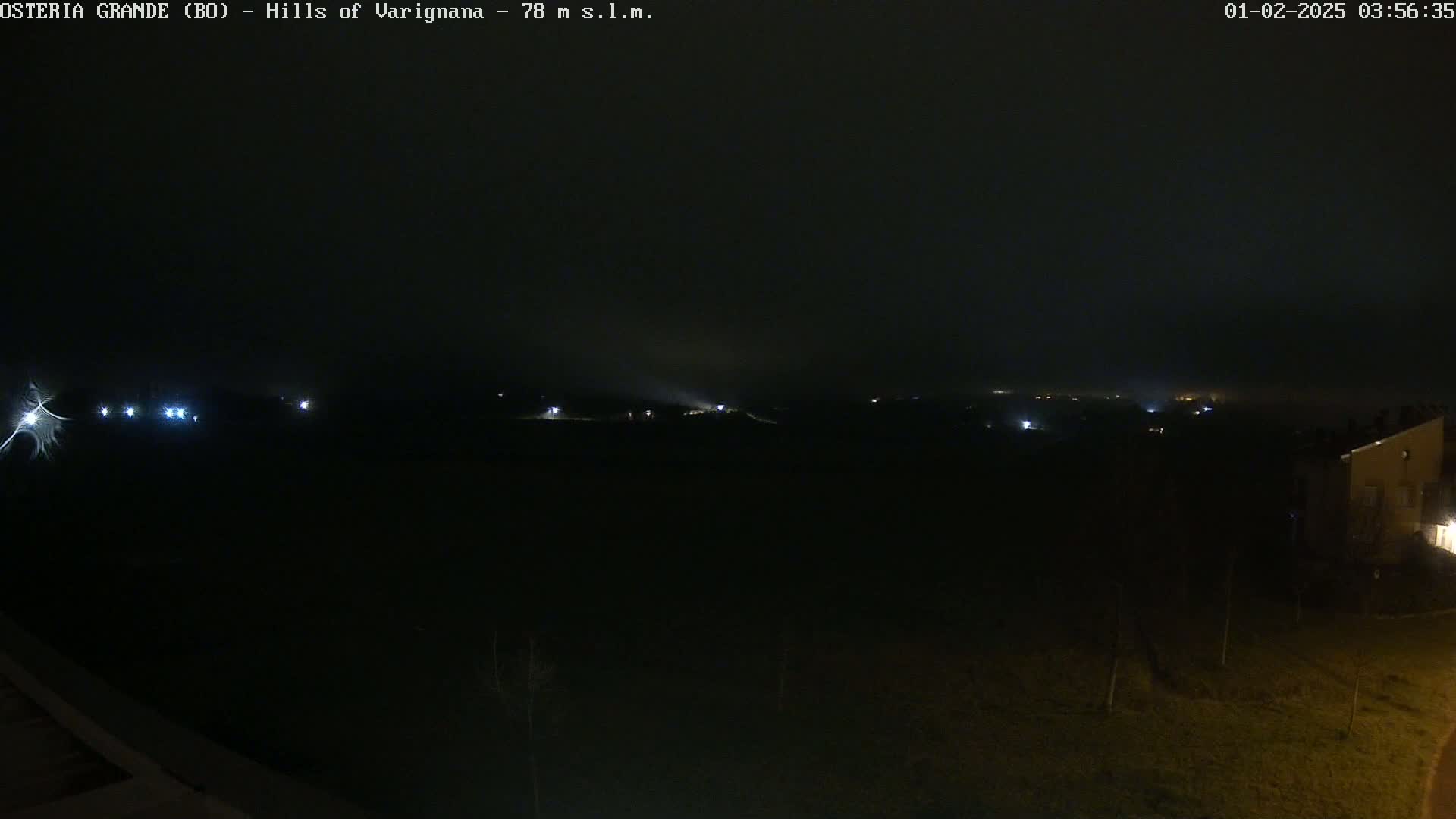A dark, nighttime landscape is visible, with a few faint lights in the distance and a foggy or hazy atmosphere.