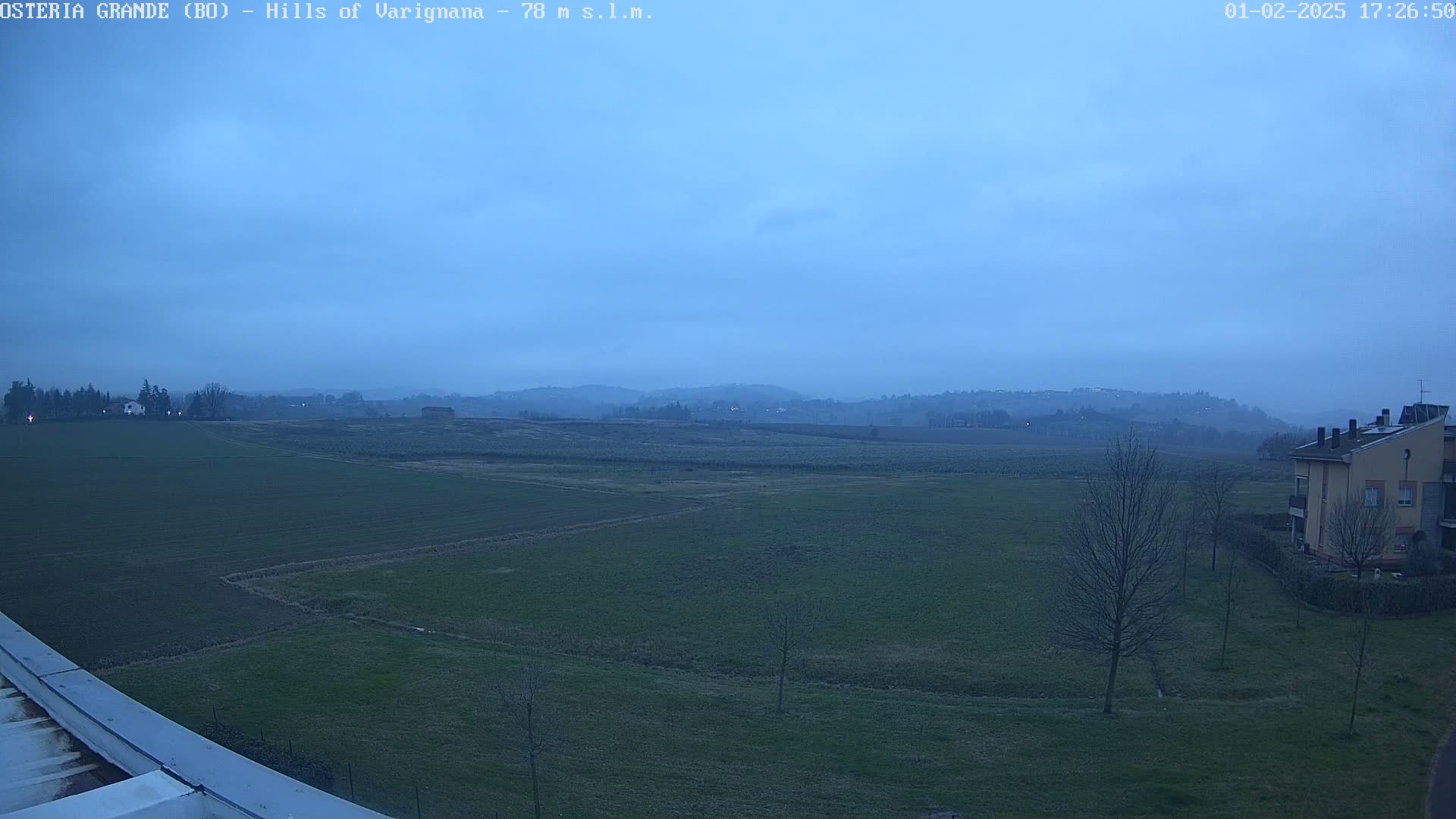 A wide, flat expanse of green fields stretches to rolling hills under a dusky blue sky.