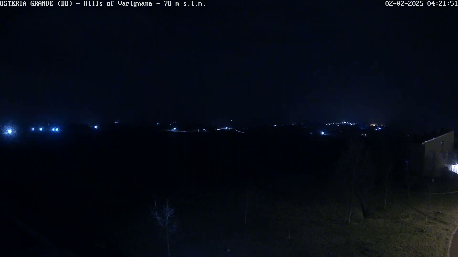 A dark, nighttime landscape shows a distant line of lights in the hills under a clear, black sky.
