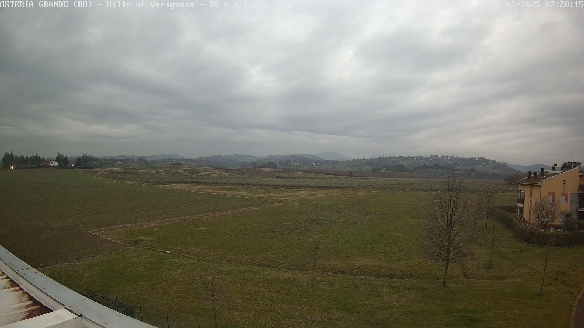 A wide, flat expanse of farmland under an overcast sky stretches to rolling hills in the distance.