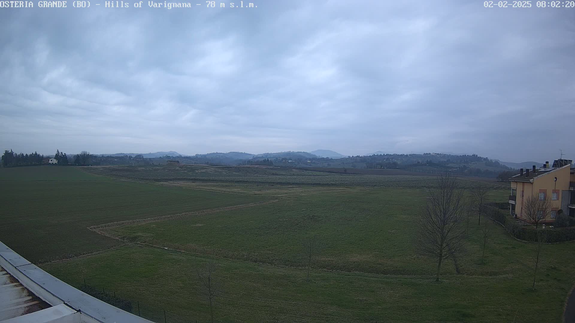 A flat, grassy landscape under an overcast sky shows distant hills and a few buildings.