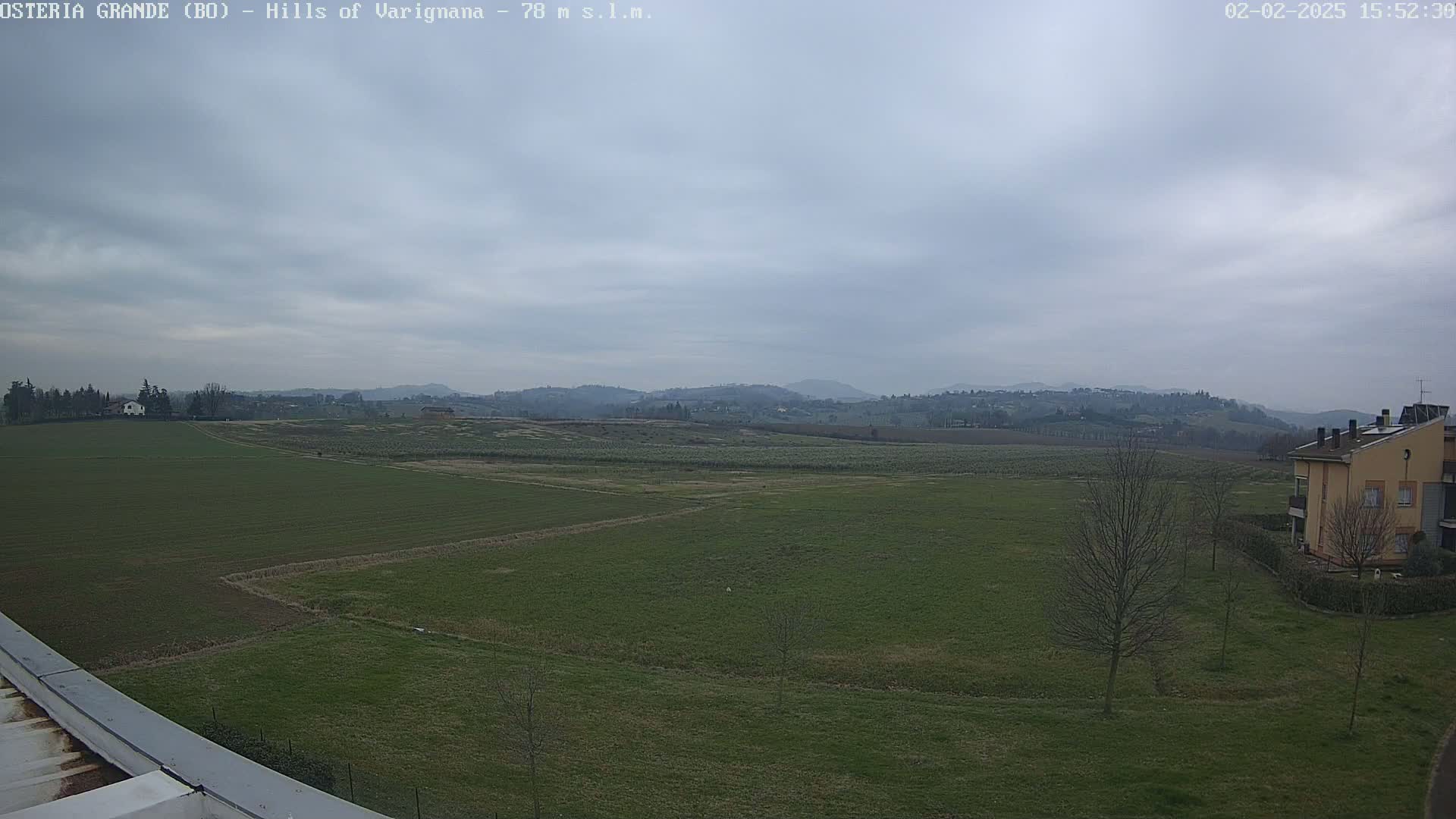 A sprawling green field stretches out to rolling hills under a cloudy sky.