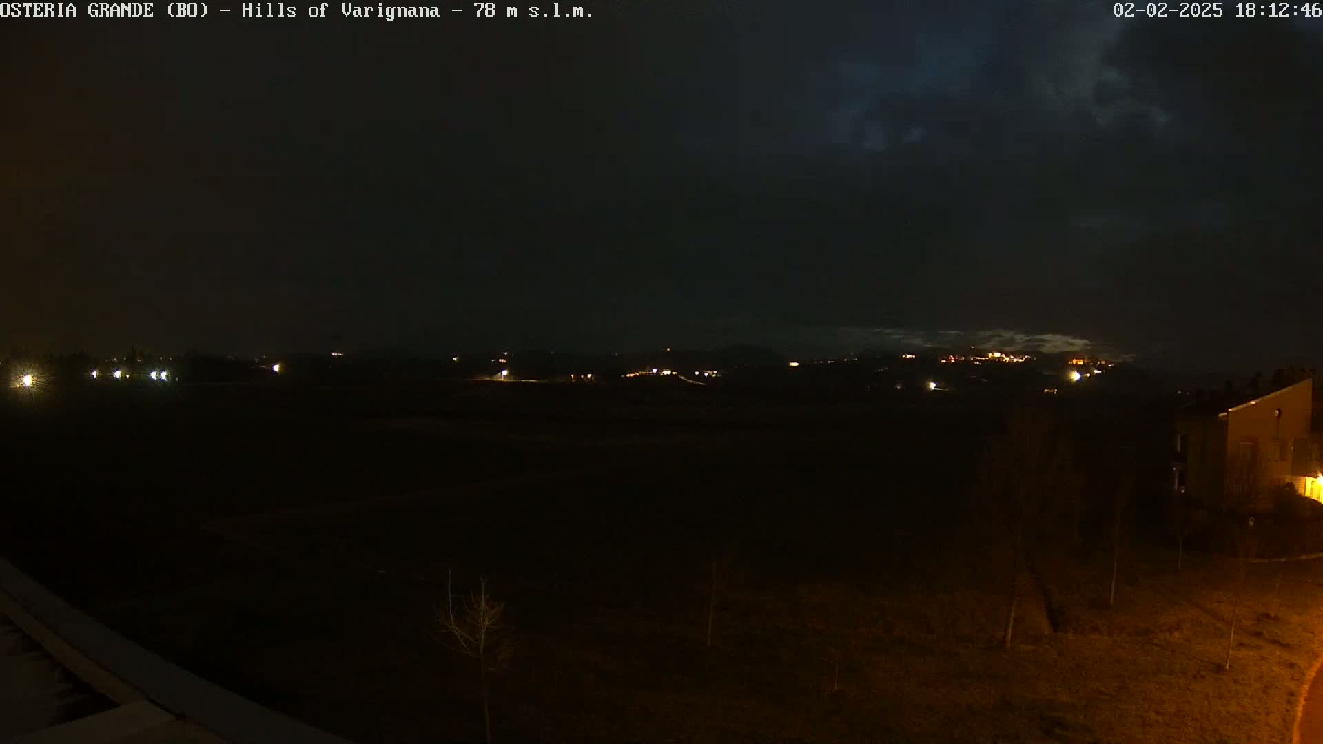A nighttime view of dimly lit hills and buildings under a dark, cloudy sky.