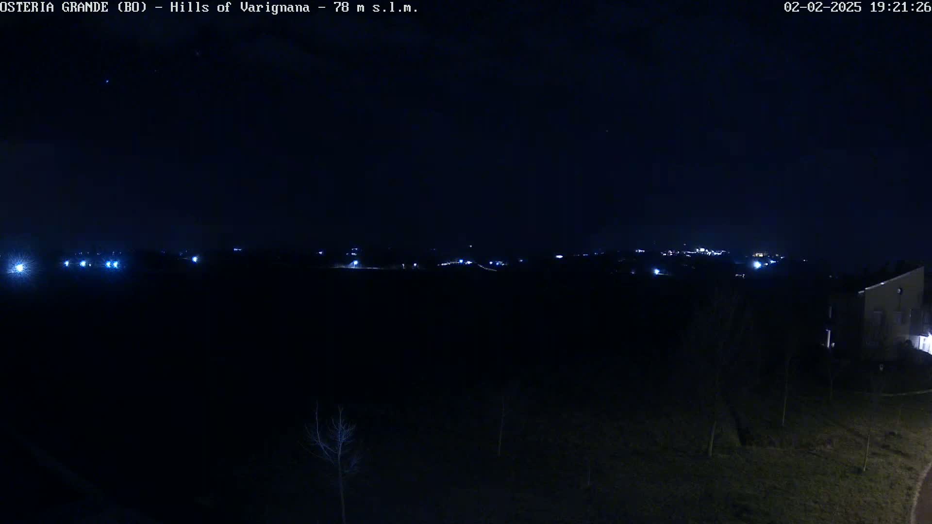 A nighttime view shows a dark landscape with a few distant lights and a building on the right, under a clear, dark sky.