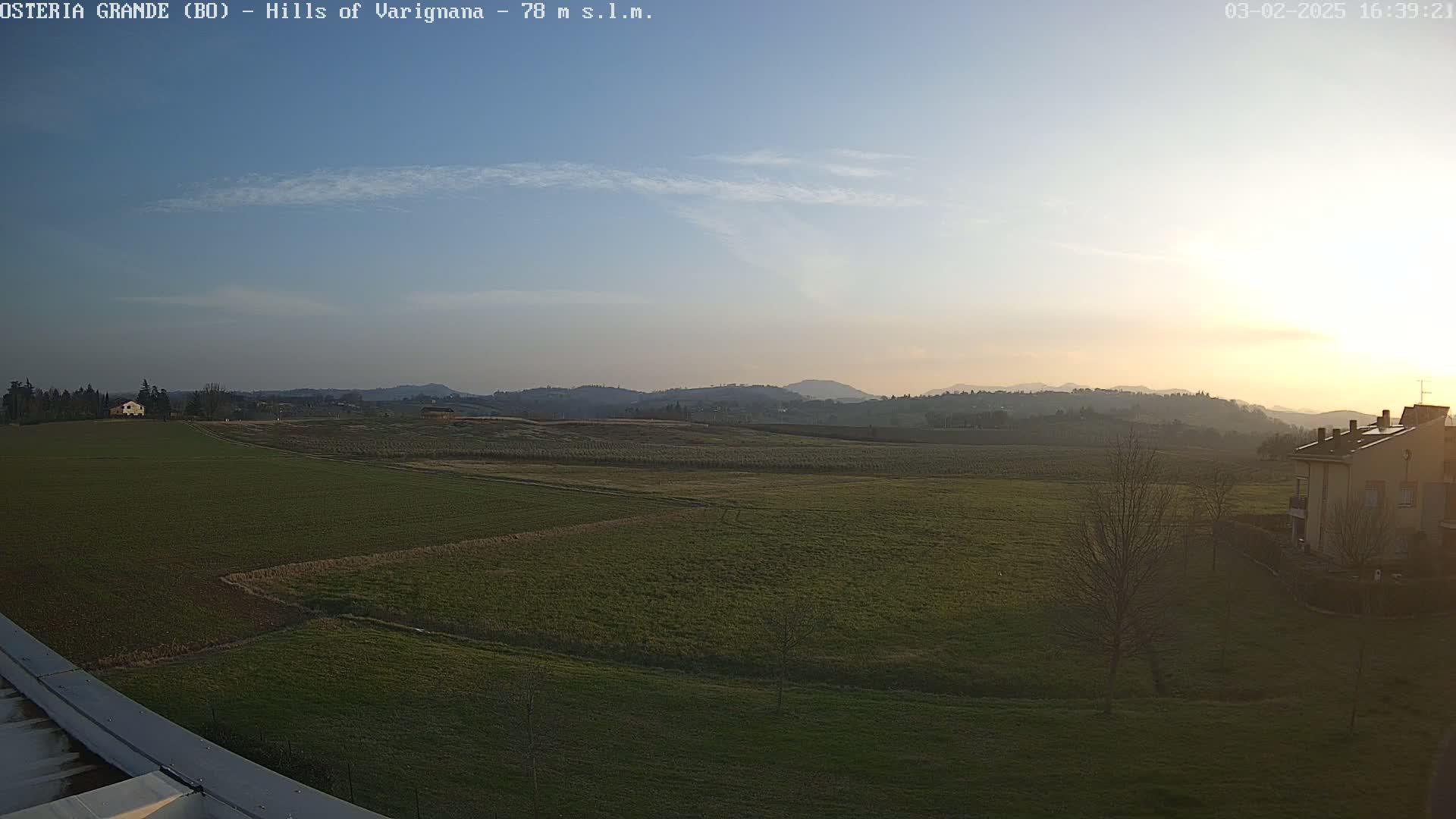A wide, flat expanse of green farmland stretches towards distant hills under a clear, sunset sky.