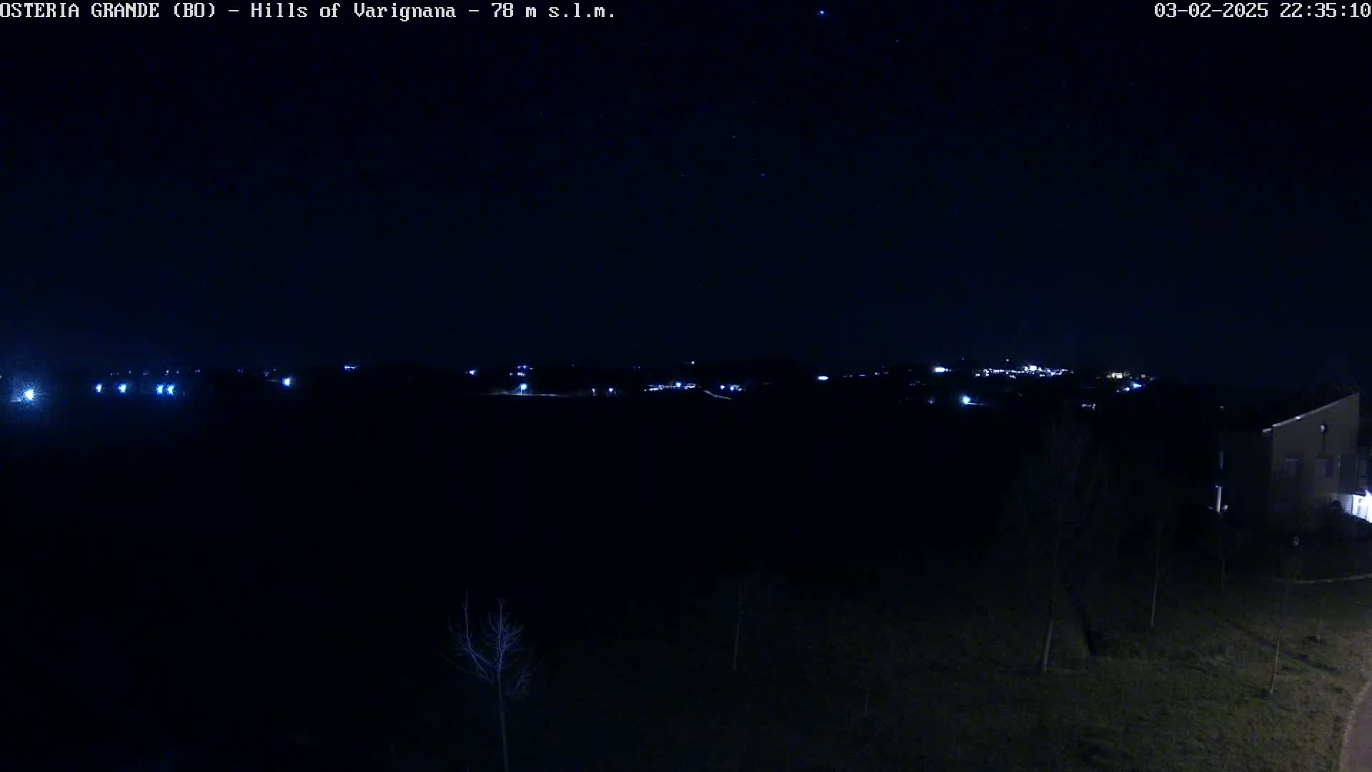 A nighttime, dark landscape shows a distant town's lights against a starlit sky.