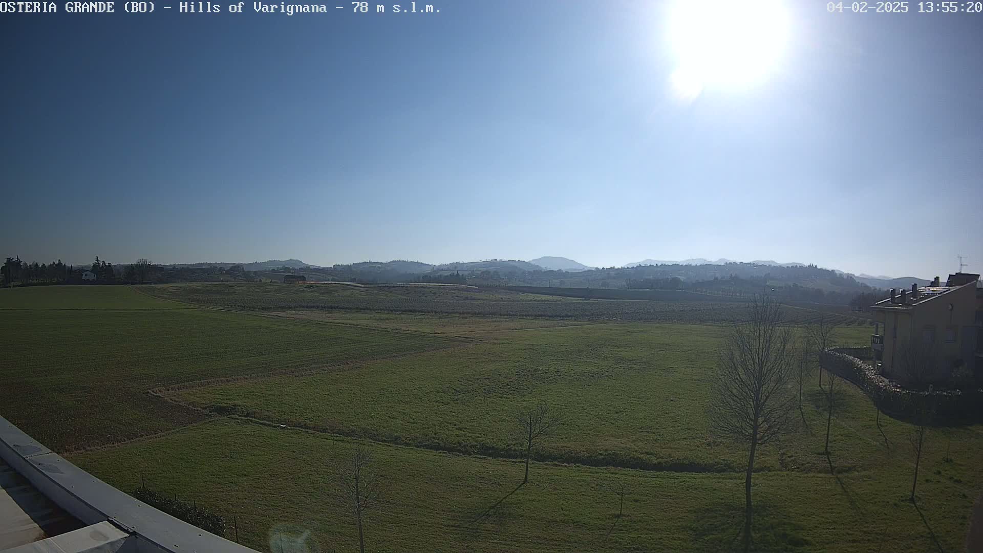 A sunny day reveals a wide expanse of green fields stretching towards distant, hazy hills under a clear blue sky.