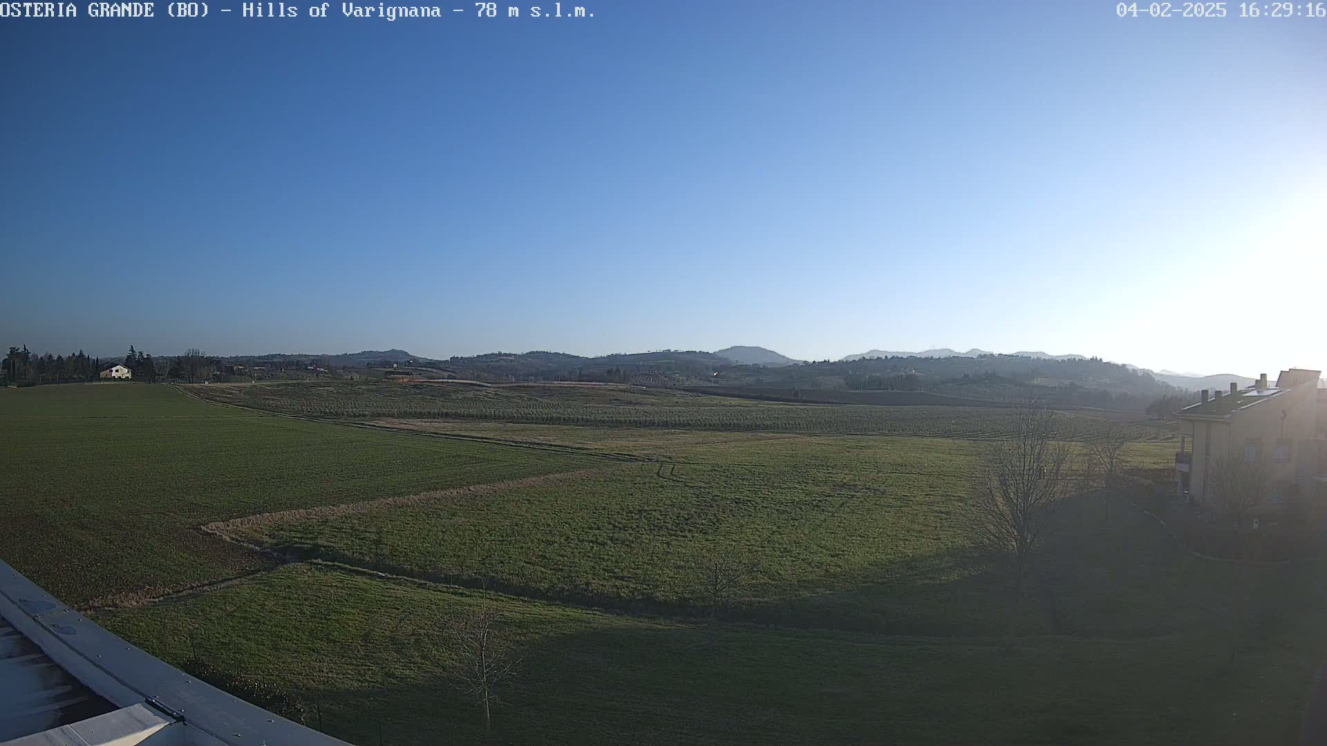 A wide, flat expanse of green farmland stretches to distant, softly-lit hills under a clear blue sky.